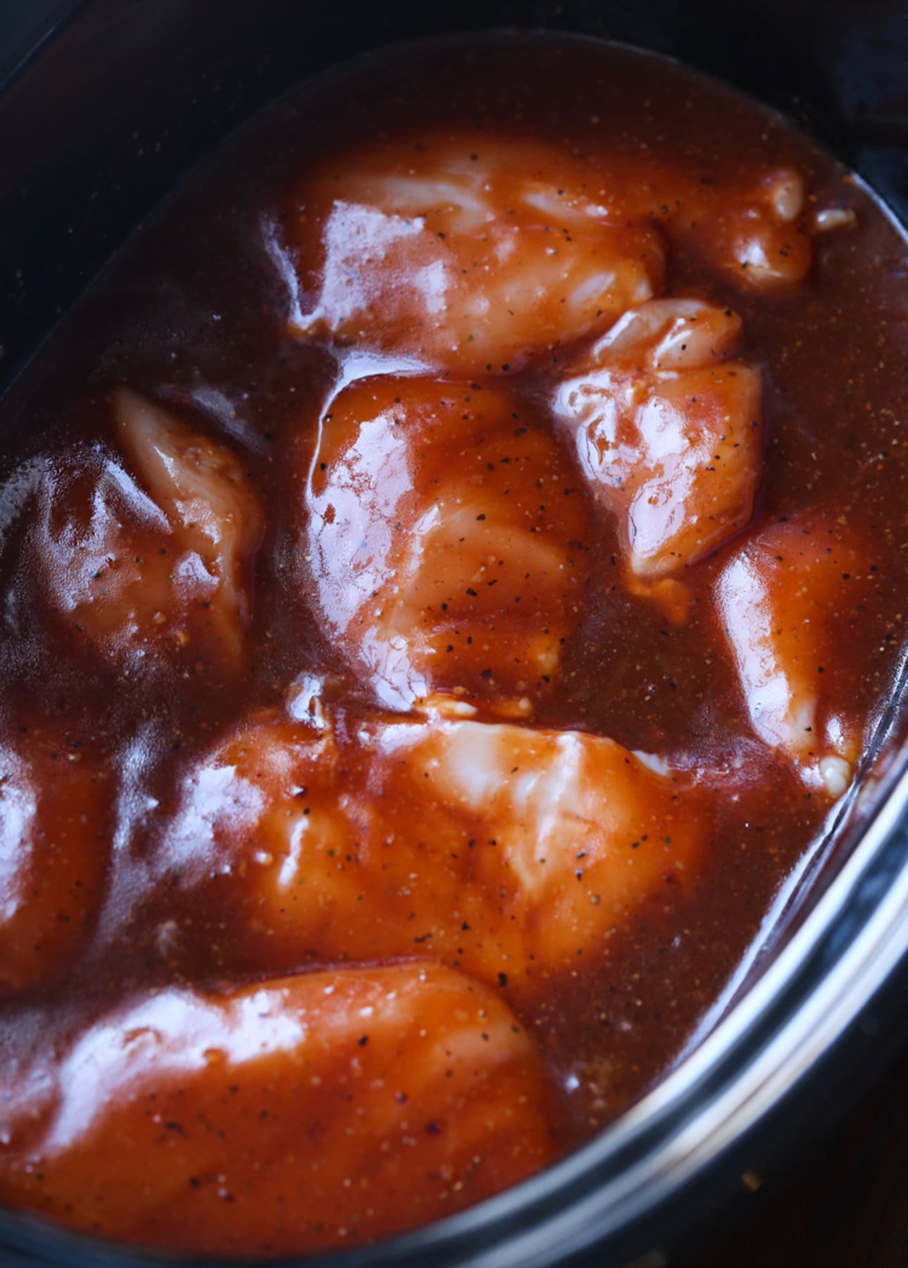 raw chicken in a crockpot slow cooker coated in BBQ sauce