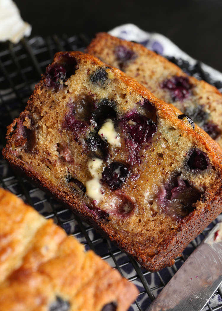 Slices of homemade blueberry banana bread laying next to a loaf.