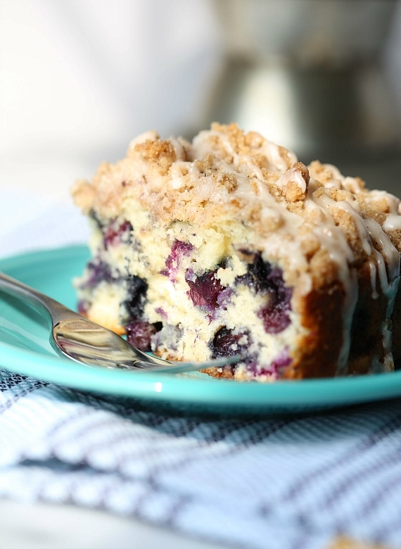 A slice of blueberry muffin cake next to a fork on a turquoise plate.