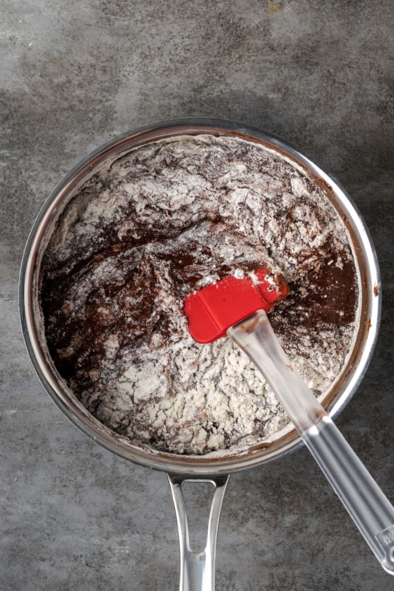 Flour stirred into brownie batter in a saucepan.