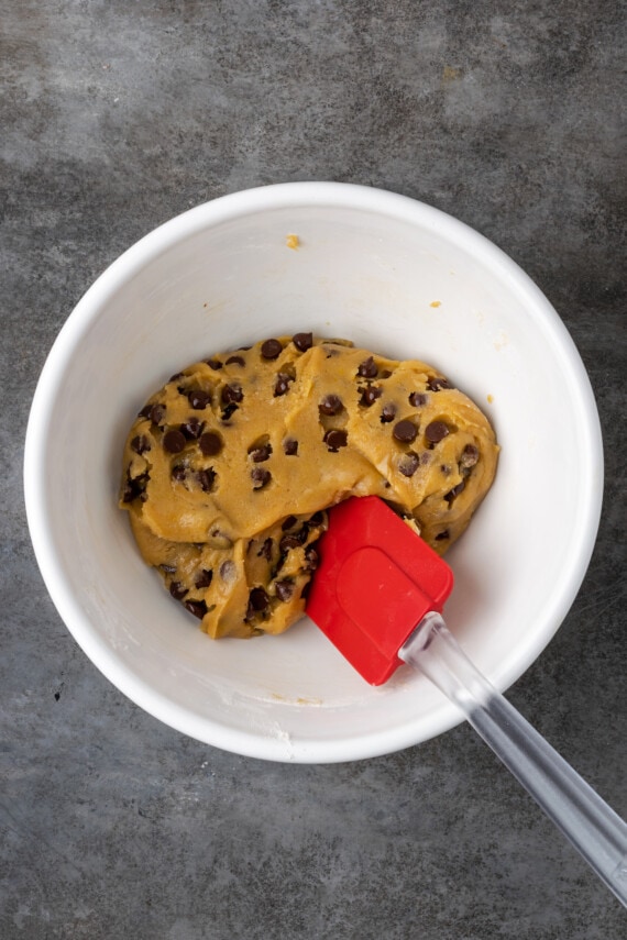 Chocolate chips stirred into cookie dough in a white bowl.