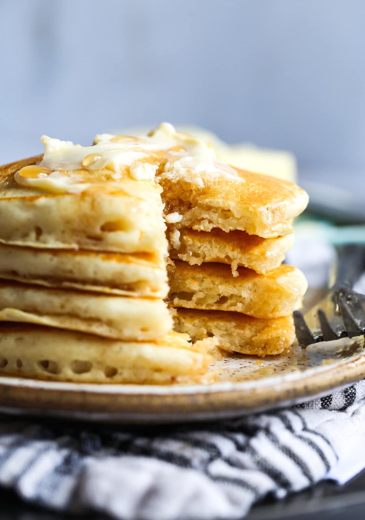 Buttermilk pancakes stacked on a plate with butter and syrup cut into showing the fluffy interior