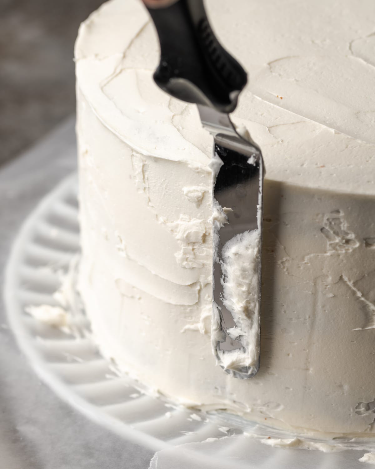 An offset spatula smoothes the frosting on the side of a cannoli cake.