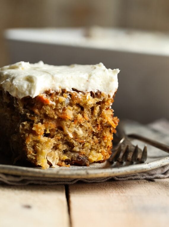 A perfectly moist and fluffy slice of frosted carrot cake on a plate next to a fork