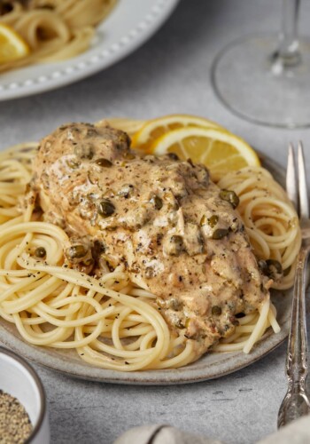 Chicken piccata served over pasta on a plate.