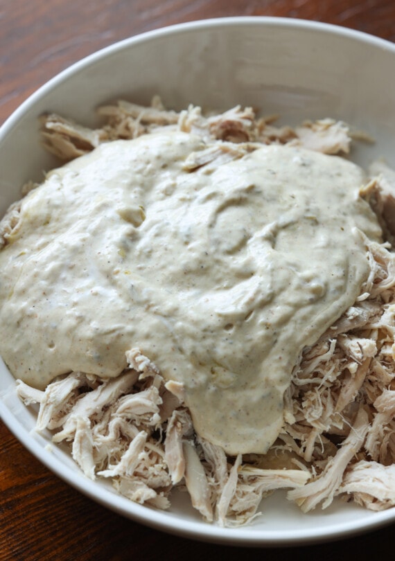 sour cream enchilada sauce poured on top of shredded chicken in a white bowl