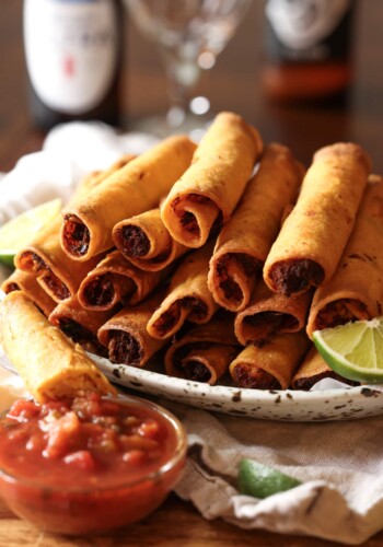 taquitos on a platter with salsa and lime wedges with beer
