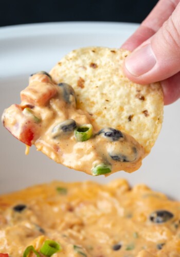 A hand holding a chip dipped in Crock Pot chicken nacho dip.