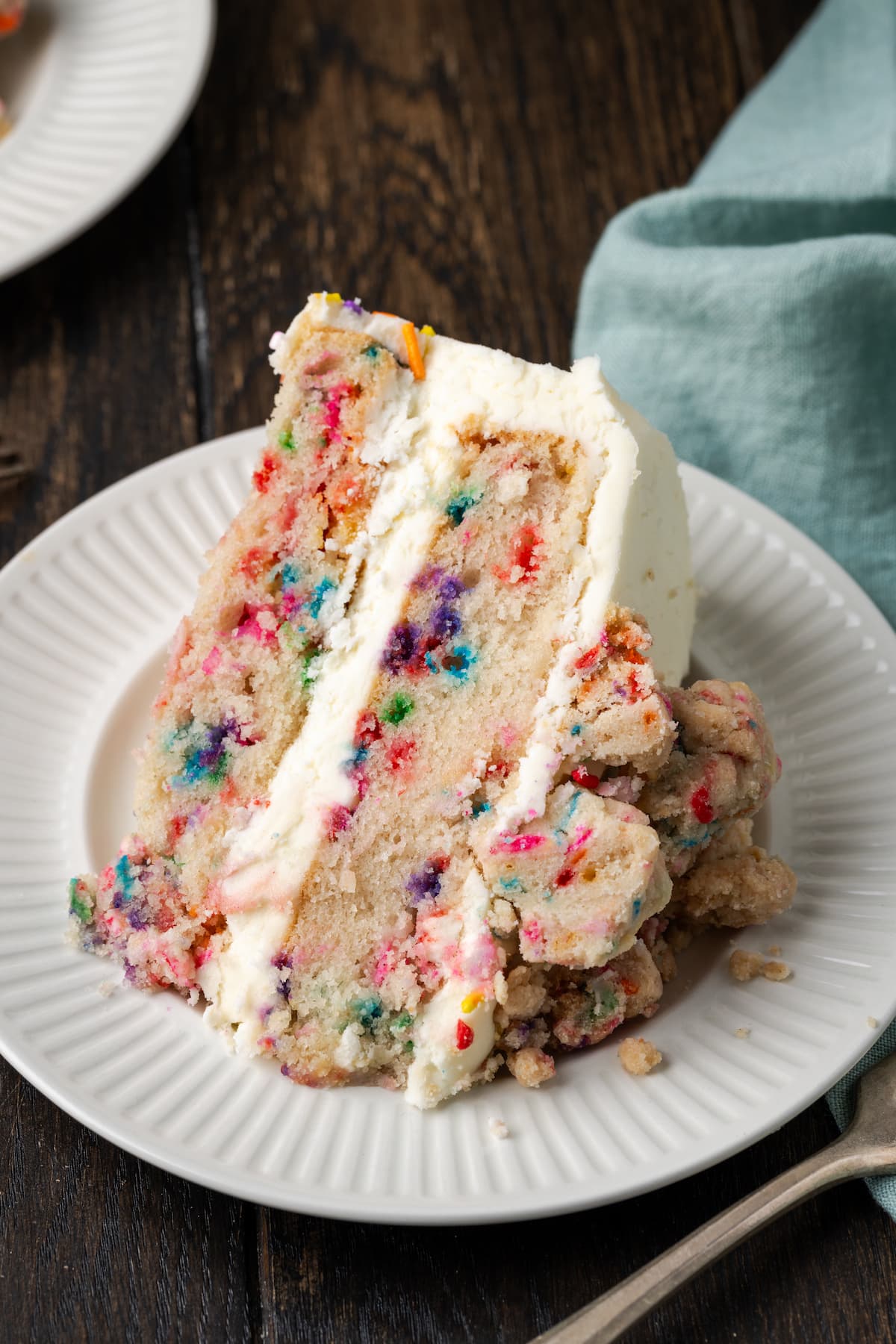 A slice of frosted confetti cake on a white plate.