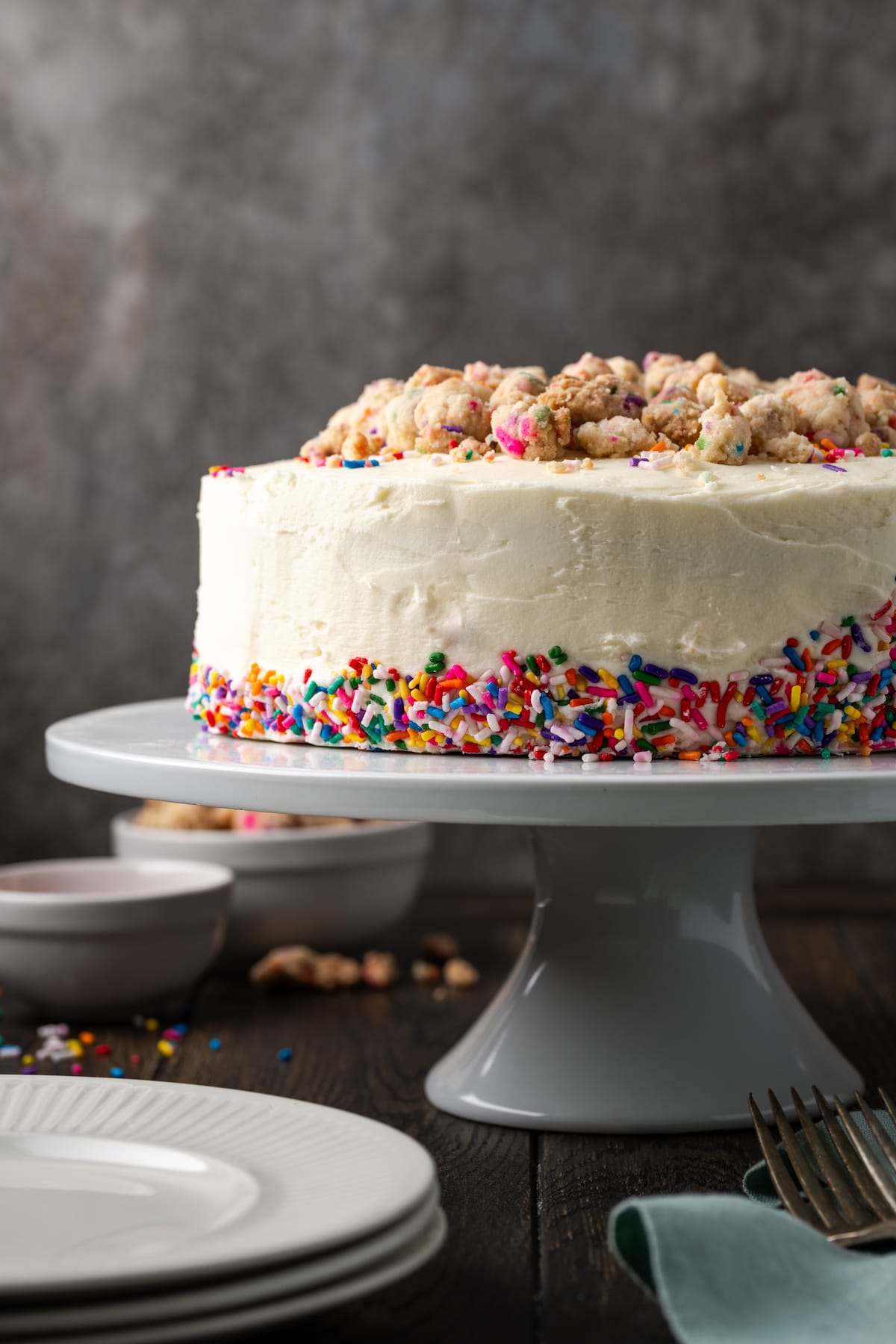 Frosted confetti cake decorated with sprinkles on a white cake stand.