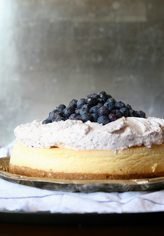 Side view of a blueberry mousse cheesecake topped with a pile of fresh blueberries.