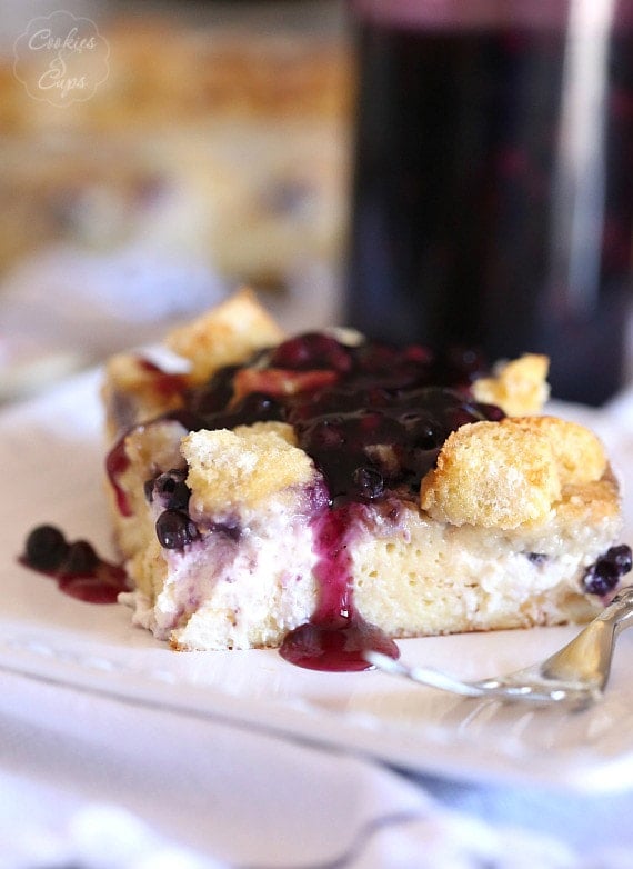 A slice of overnight blueberries and cream French toast casserole on a plate drizzled with blueberry sauce.
