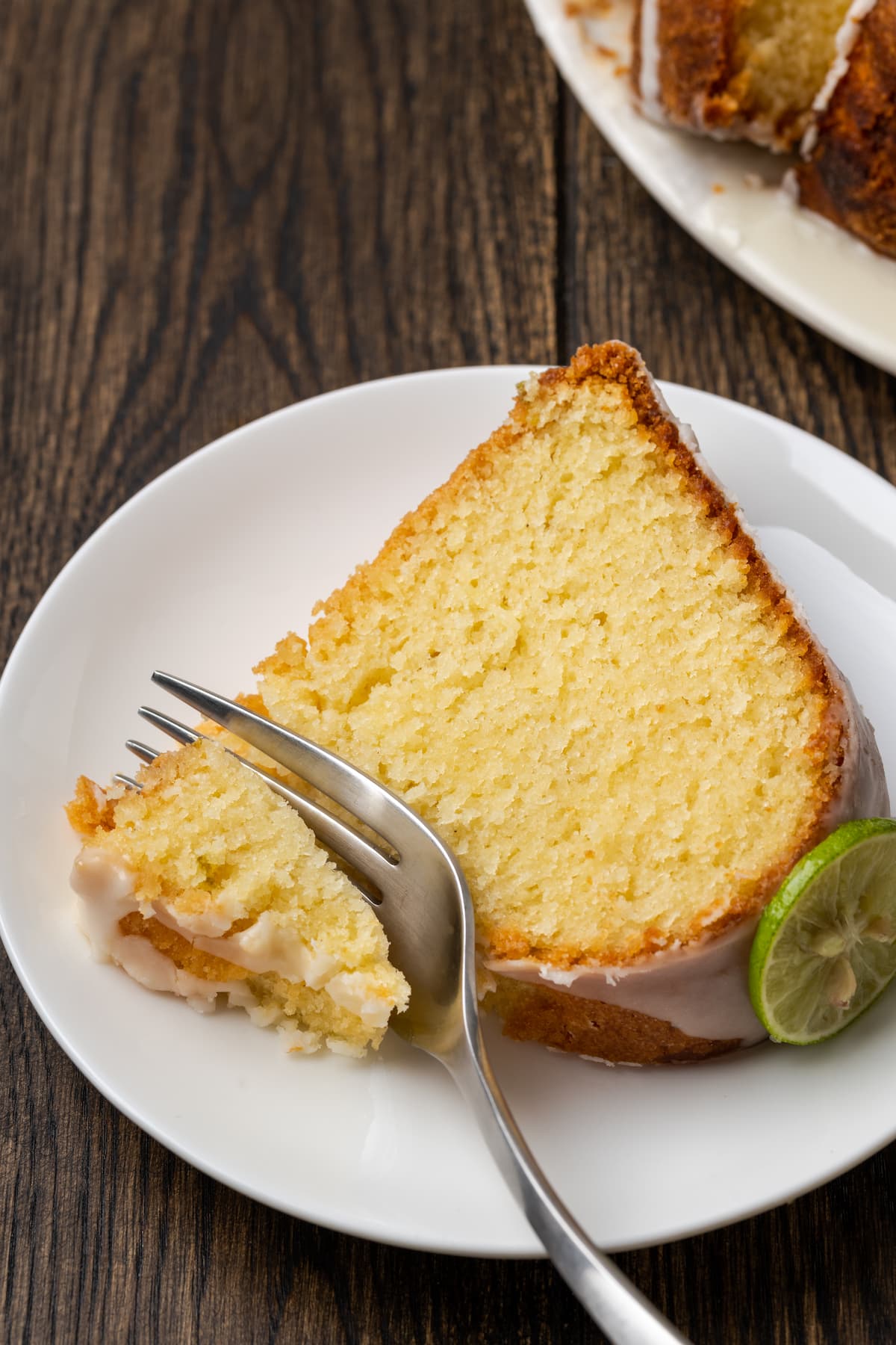 A fork cuts into the corner of a slice of Key lime pound cake on a white plate.