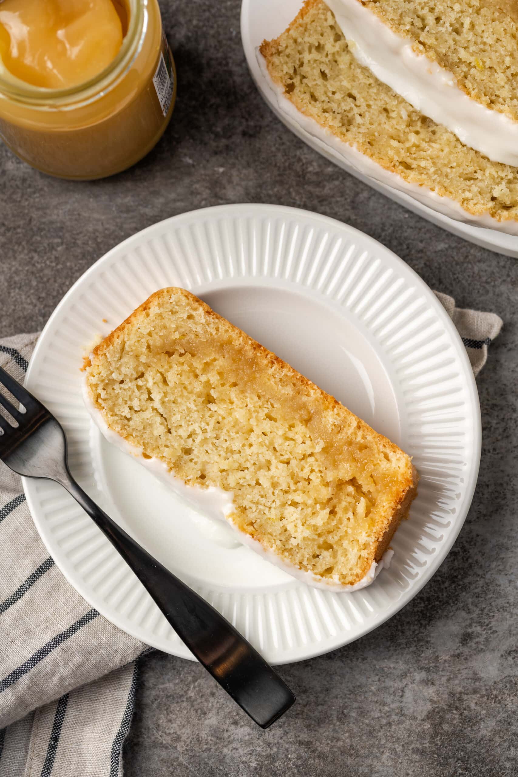 Overhead view of a slice of glazed lemon pound cake on a white plate next to a fork.