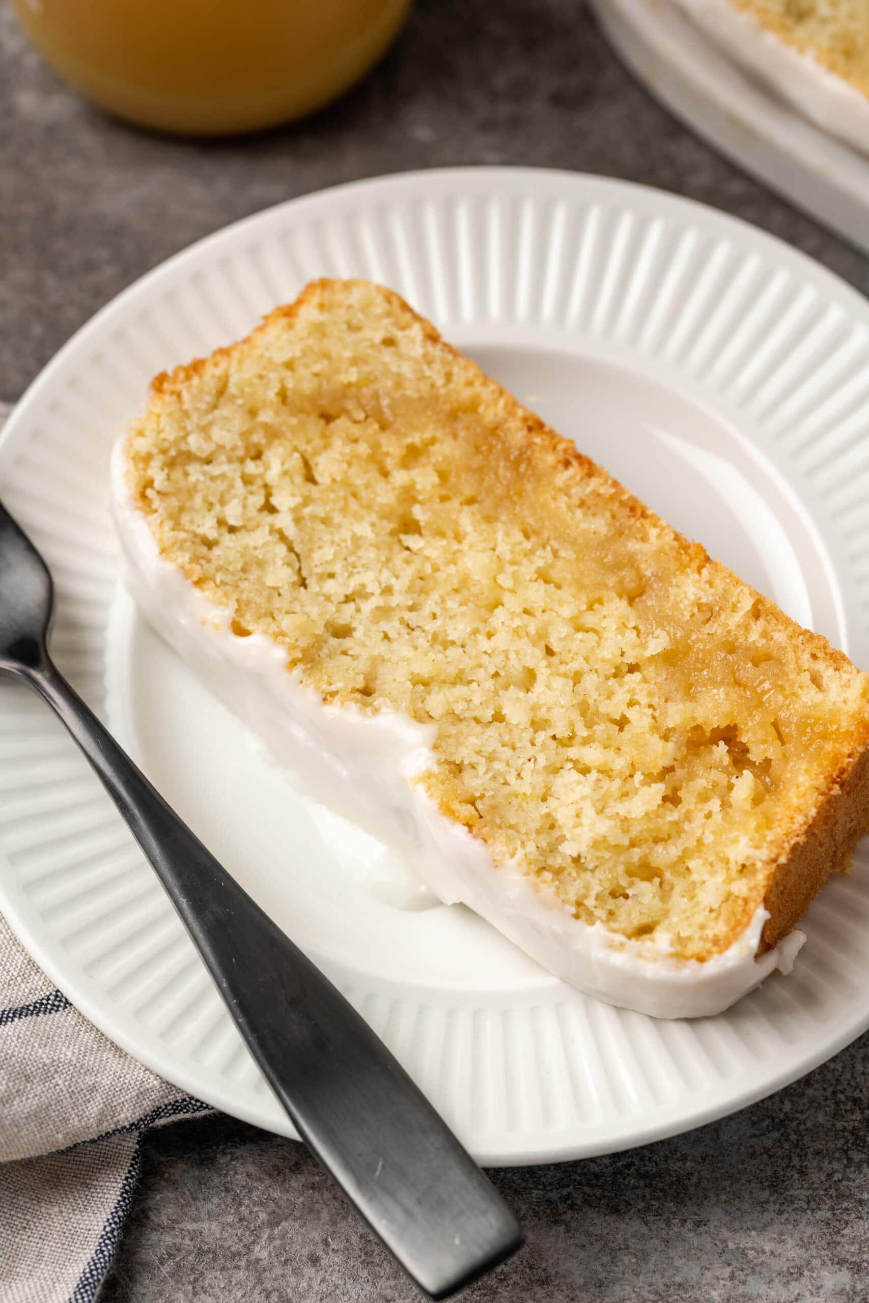 A slice of glazed lemon pound cake on a white plate next to a fork.