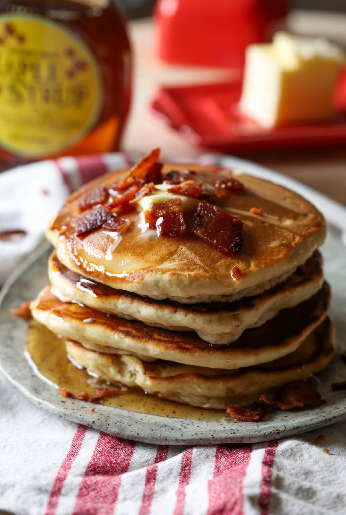 A stack of pancakes with bacon and butter on top with maple syrup dripping down the sides.