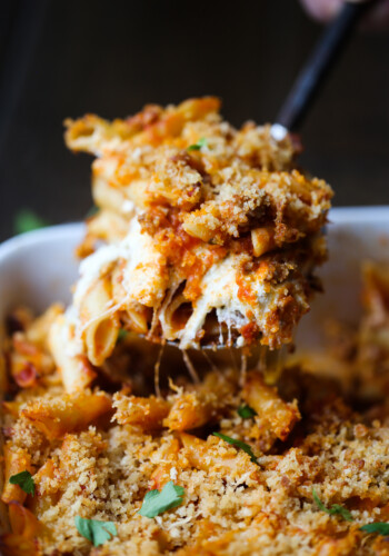 A spoonful of cheesy baked mostaccioli is served from a casserole dish.