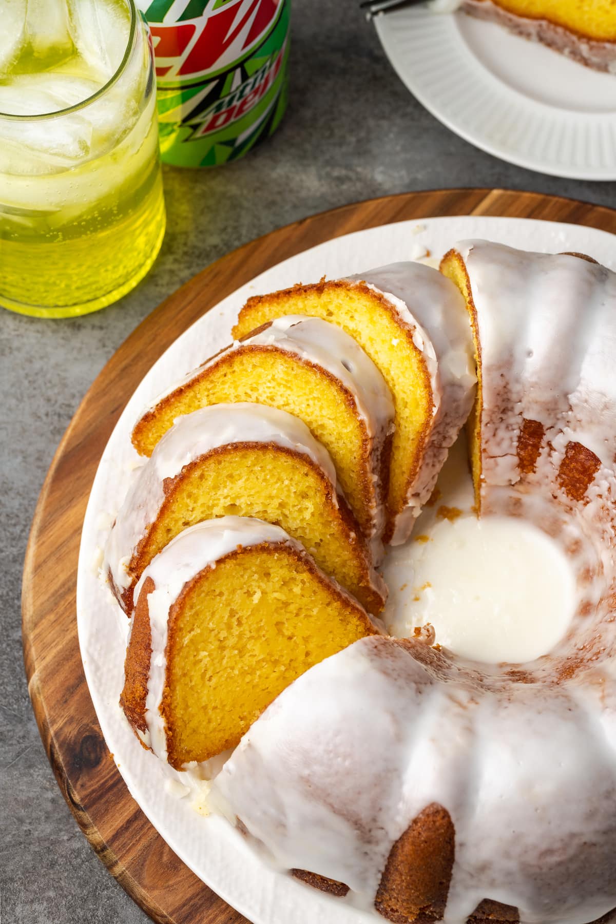 Glazed Mountain Dew bundt cake cut into slices on a plate, next to a glass of Mountain Dew.