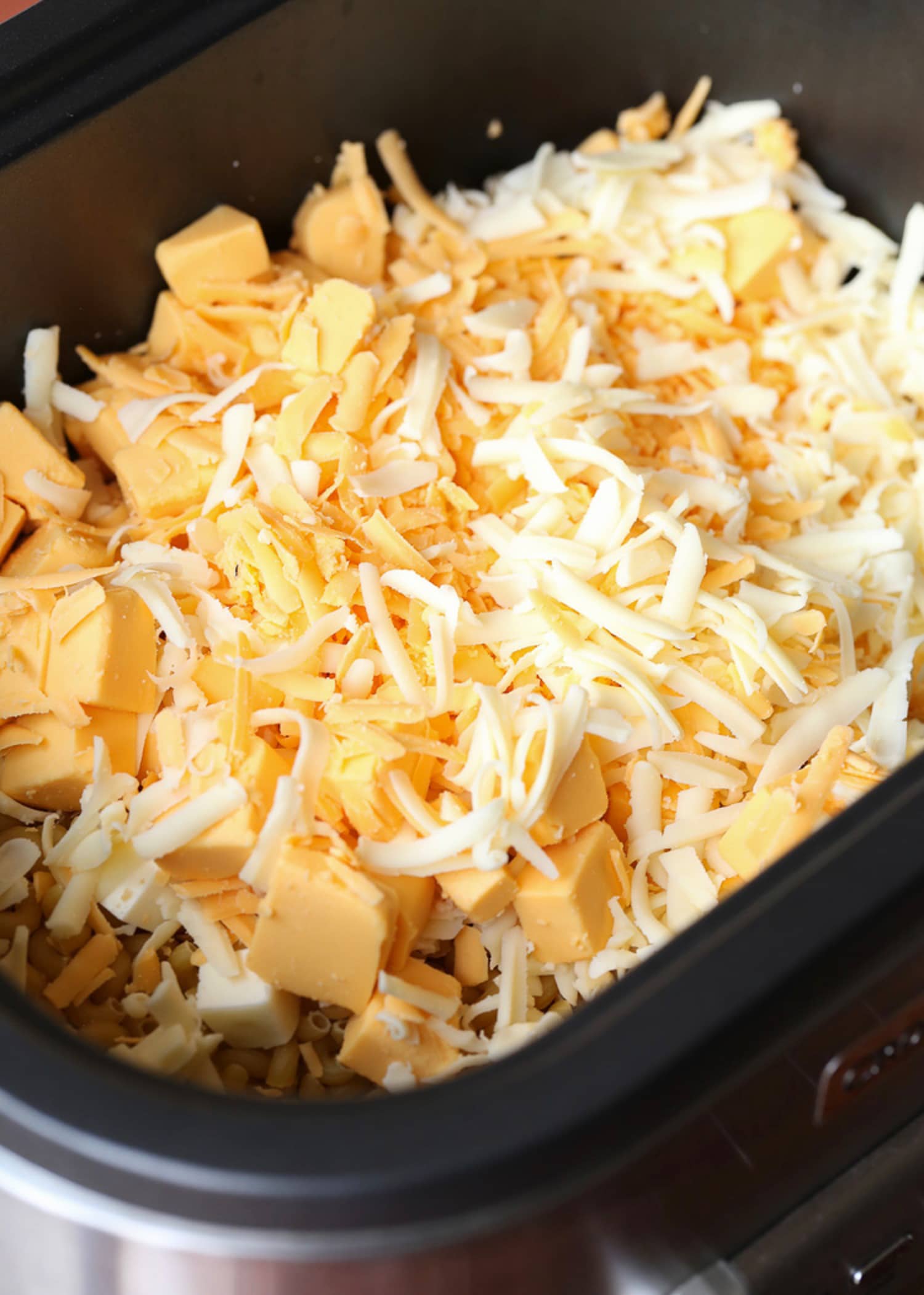 Grated cheese on top of pasta in a slow cooker prepping mac and cheese