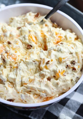 A close up image of bowl of orange cream fruit salad topped with chopped pecans.