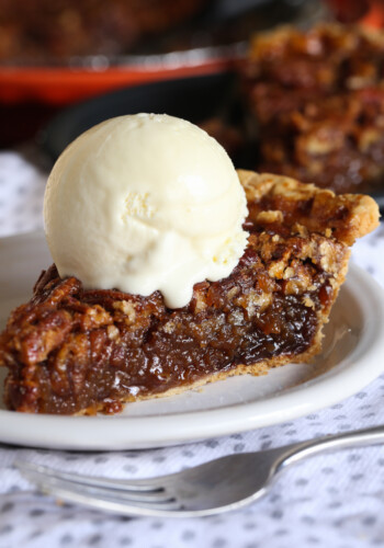 A slice of pecan pie on a white plate topped with a scoop of vanilla ice cream.