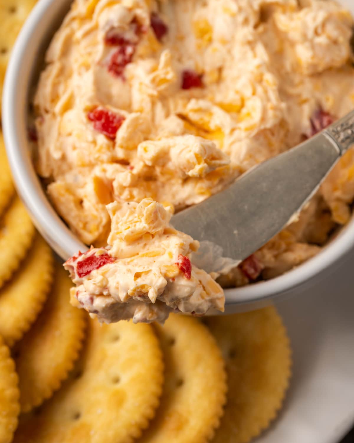 Close up of a bowl of pimento cheese served with a cheese knife on a platter of crackers.