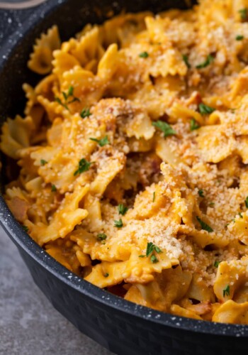 Creamy pumpkin pasta with bacon in a large black serving bowl.
