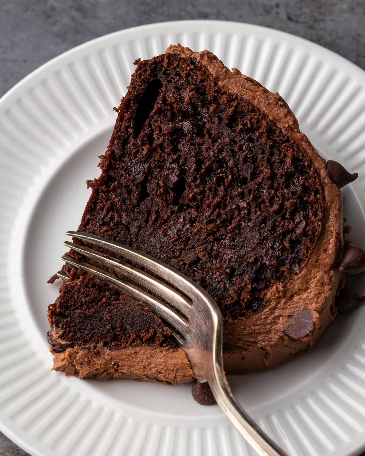 A fork cutting into a slice of ridiculous chocolate cake on a white plate.