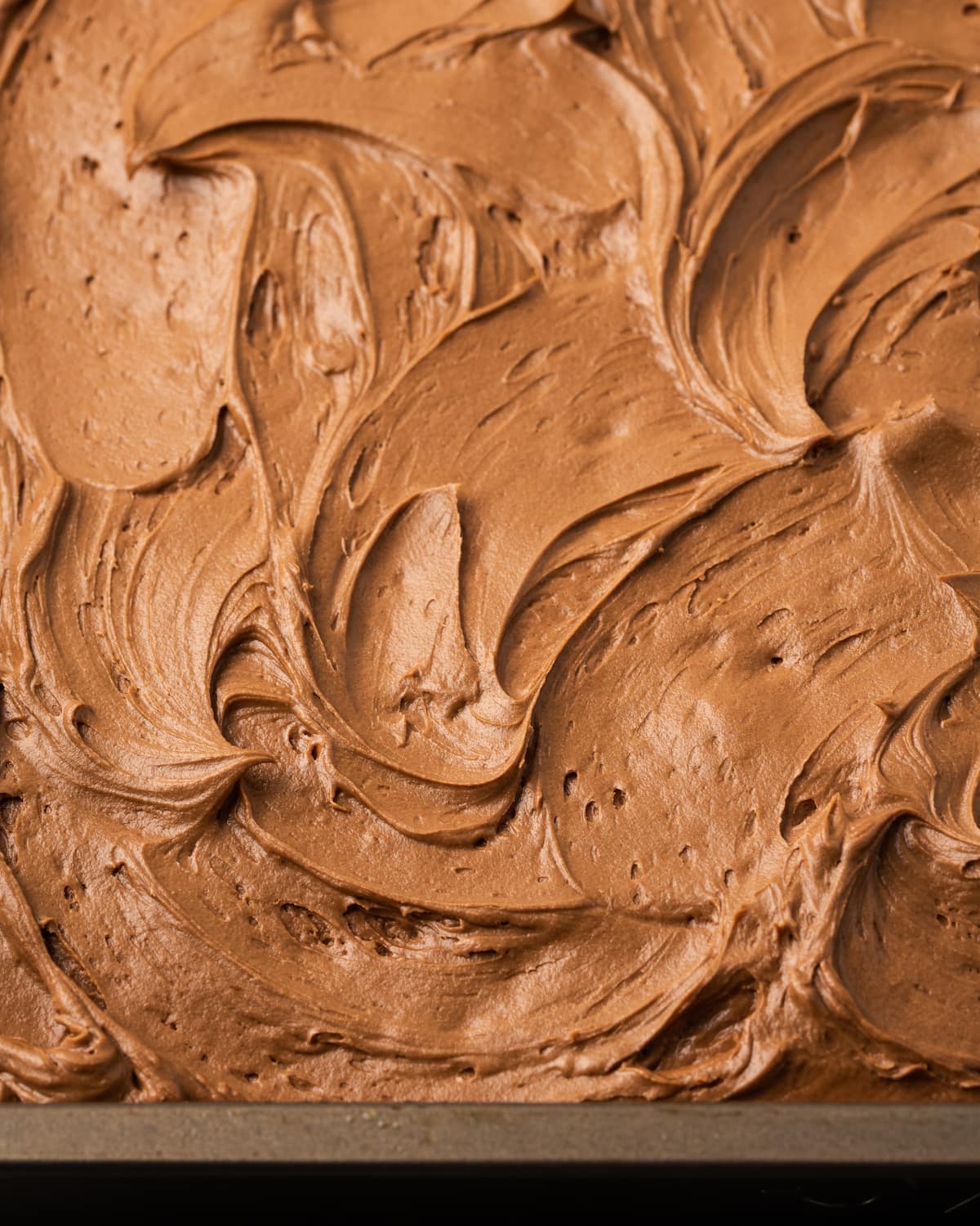 Creamy chocolate frosting spread over a sour cream cake in a baking pan.