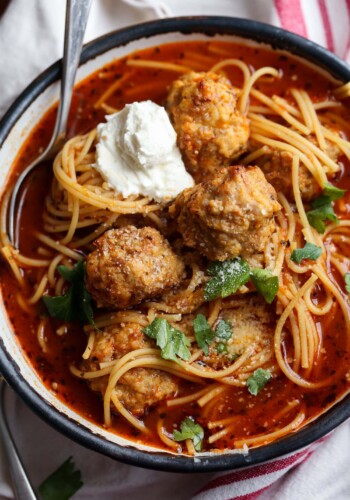 Bowl of spaghetti and meatball soup topped with parmesan cheese and ricotta