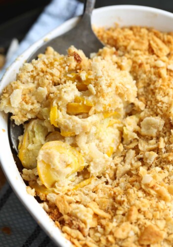 Top view of creamy squash casserole topped with crushed Ritz crackers in a baking dish with a serving spoon.