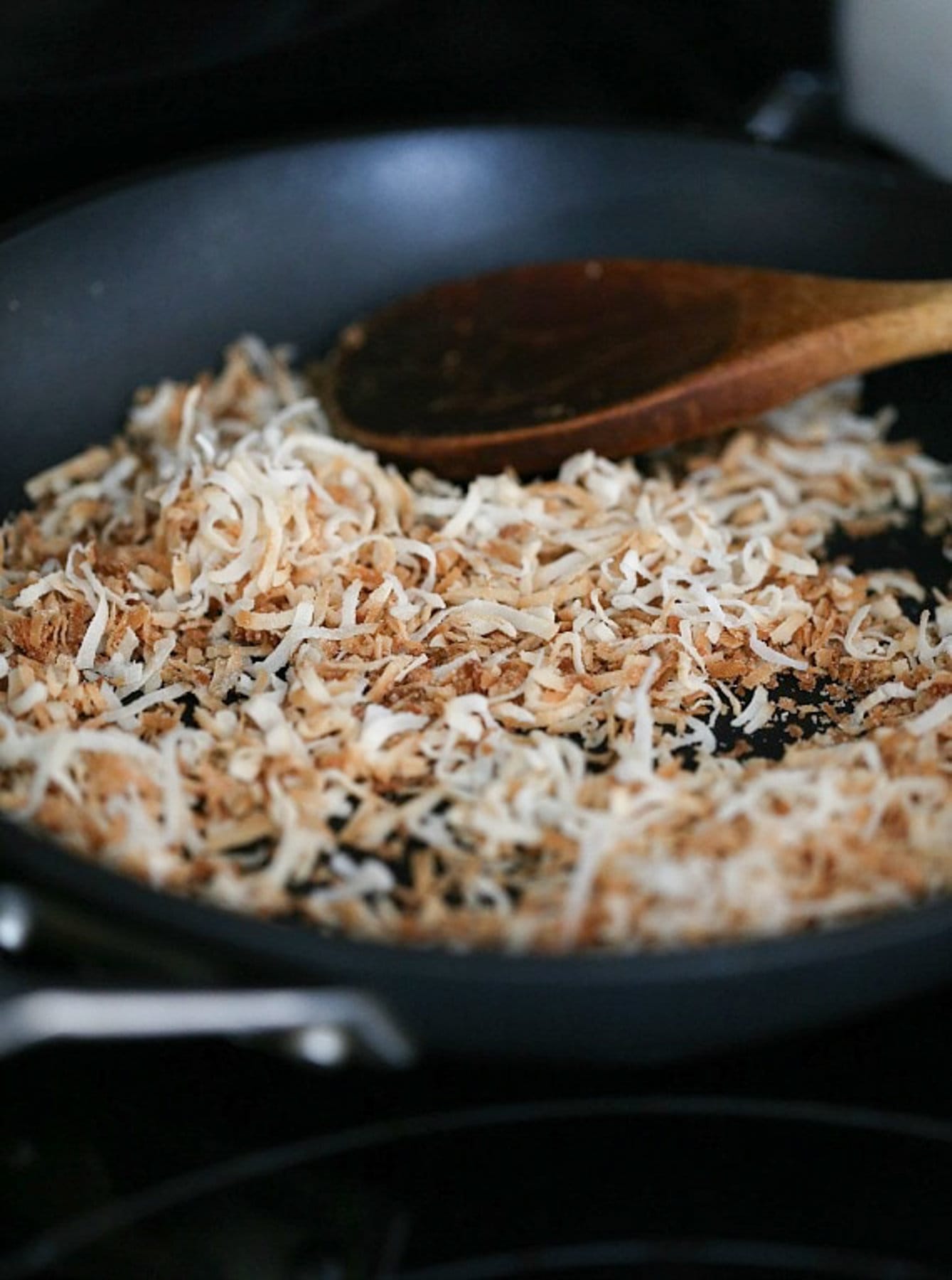 Toasted coconut in a nonstick skillet with a wooden spoon