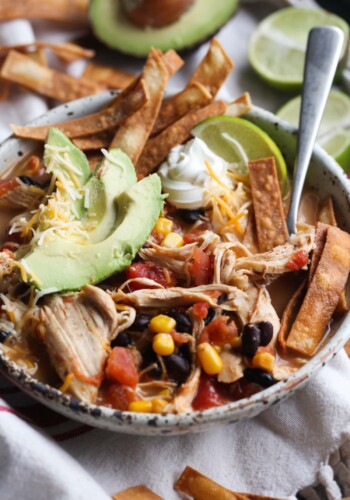 Chicken Tortilla Soup in a serving bowl with tortilla strips, avocado, a lime wedge and a spoon
