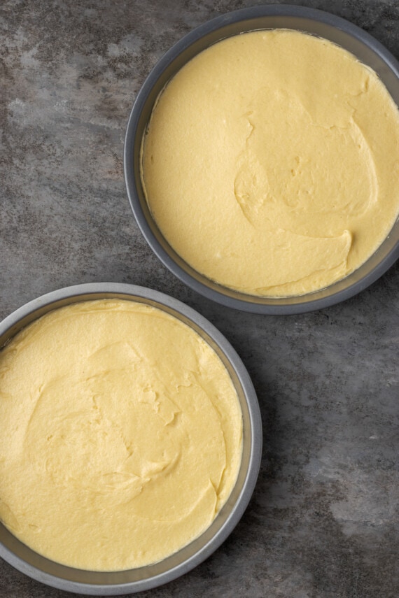 Overhead view of two round cake pans filled with sponge cake batter.